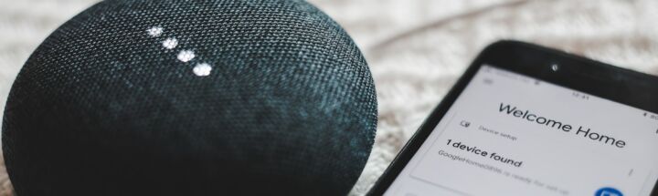 turned-on charcoal Google Home Mini and smartphone