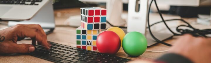 person using computer and two Rubik's Cube near monitor
