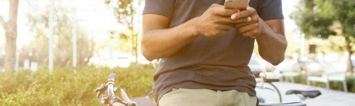 man holding smartphone leaning on bicycle during daytime