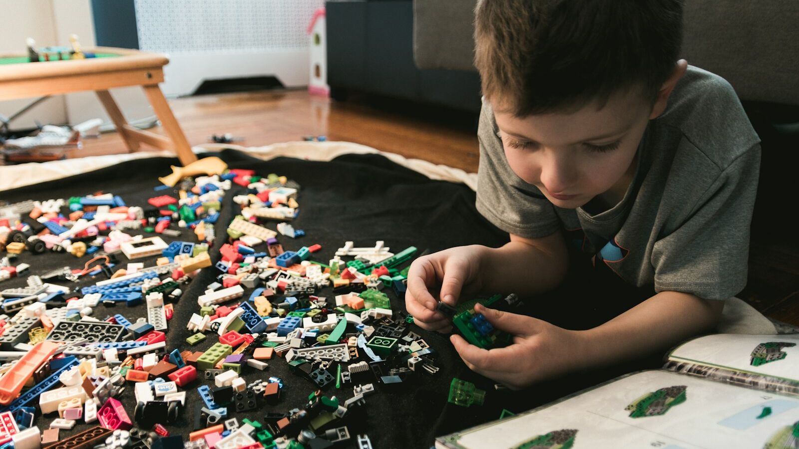 boy in grey crew-neck t-shirt plays LEGO bricks with white manual book