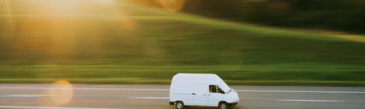 a white van driving down a road next to a lush green field