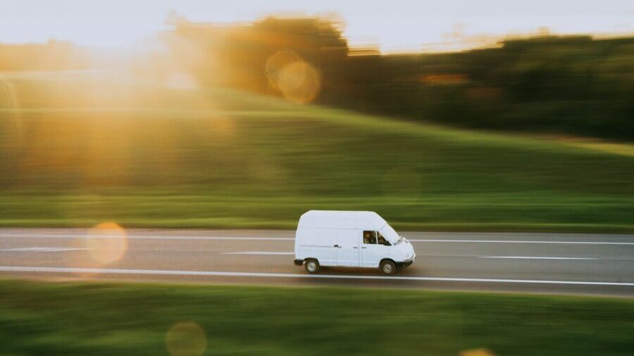 a white van driving down a road next to a lush green field