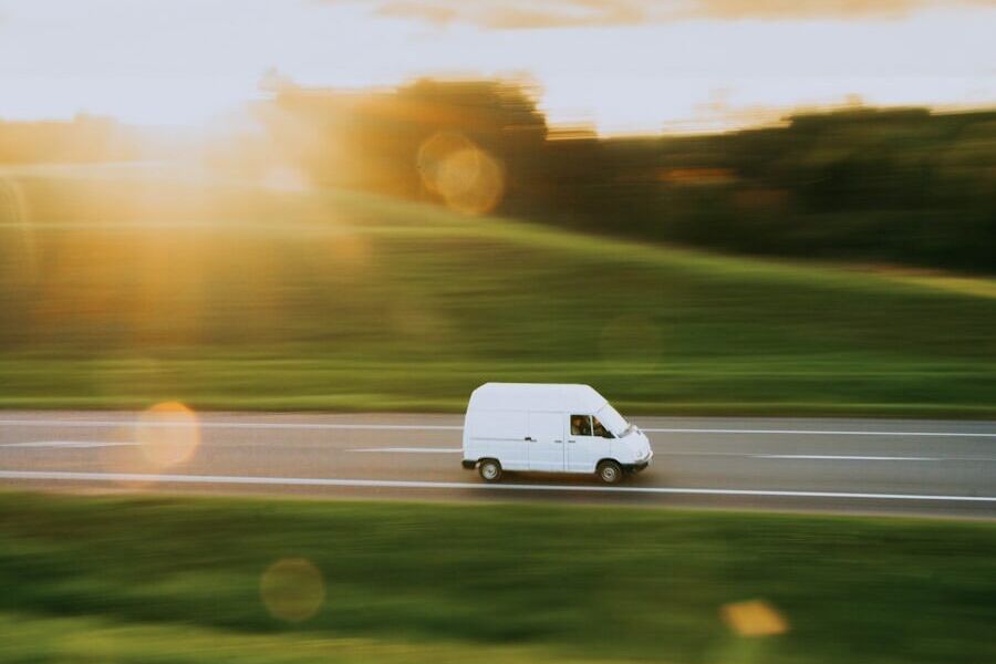 a white van driving down a road next to a lush green field