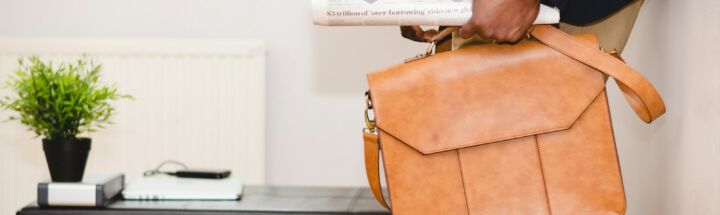 man holding brown leather bag leaning on white wall