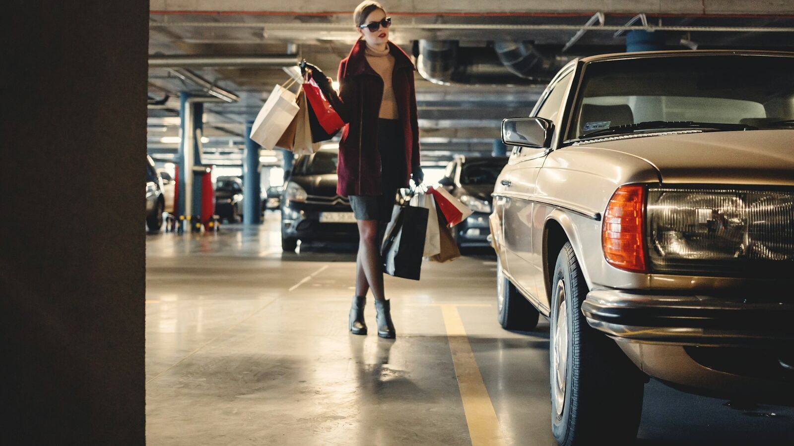 woman carrying shopping paper bags walking towards beige car inside parking lot