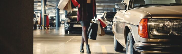 woman carrying shopping paper bags walking towards beige car inside parking lot