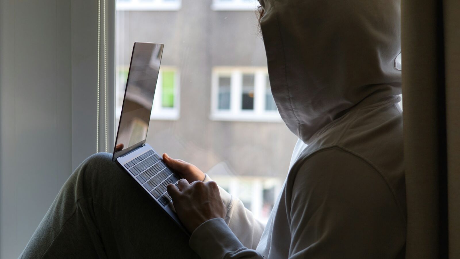 a person sitting on a window sill using a laptop