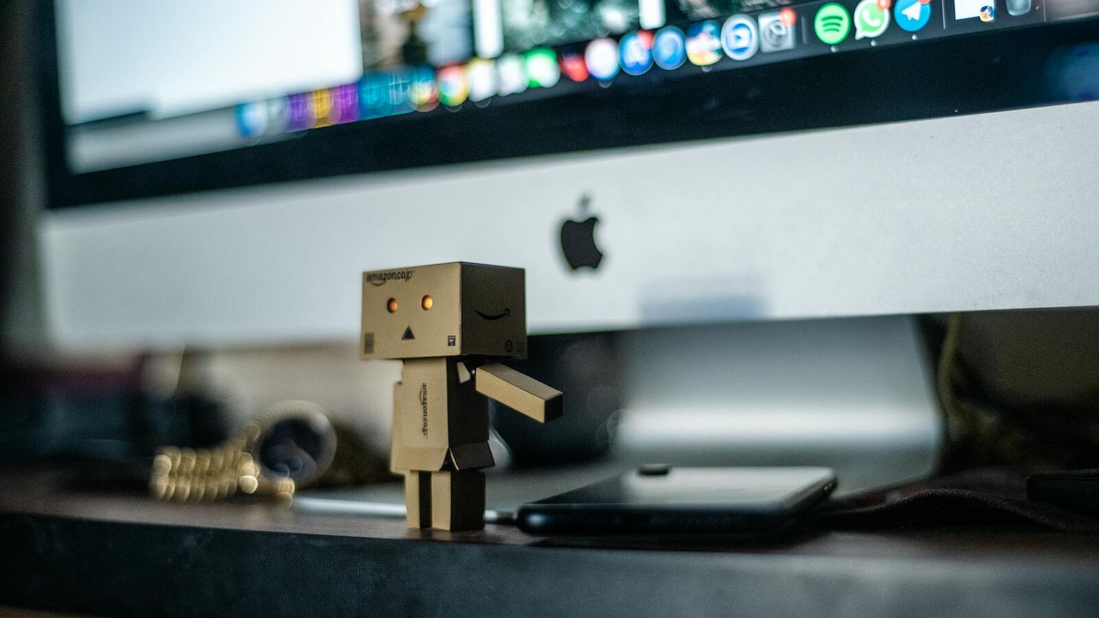A small cardboard robot toy displayed in front of a computer screen, adding charm to the workspace.