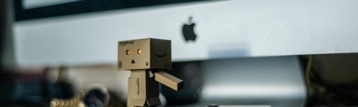 A small cardboard robot toy displayed in front of a computer screen, adding charm to the workspace.
