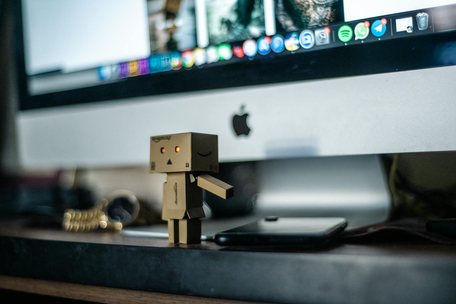 A small cardboard robot toy displayed in front of a computer screen, adding charm to the workspace.