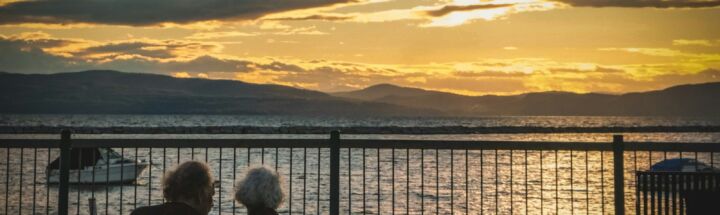 silhouette of 2 people sitting on bench near body of water during sunset
