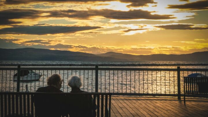 silhouette of 2 people sitting on bench near body of water during sunset