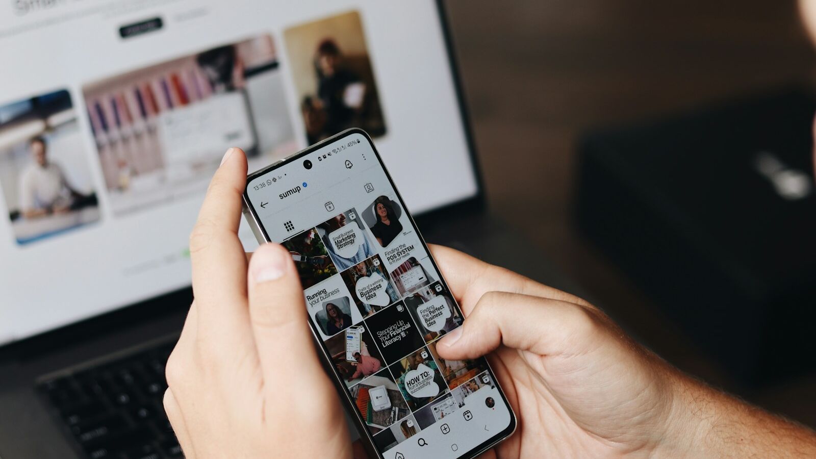 A person holding a cell phone in front of a laptop