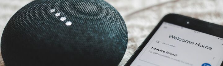 turned-on charcoal Google Home Mini and smartphone