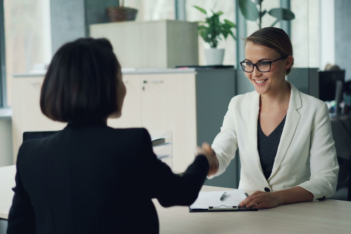 Two women shaking hands across a desk