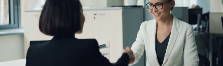 Two women shaking hands across a desk