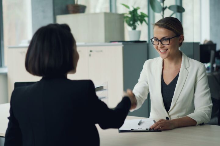 Two women shaking hands across a desk