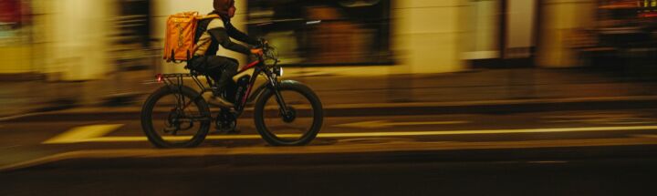 Delivery person rides bicycle through city at night