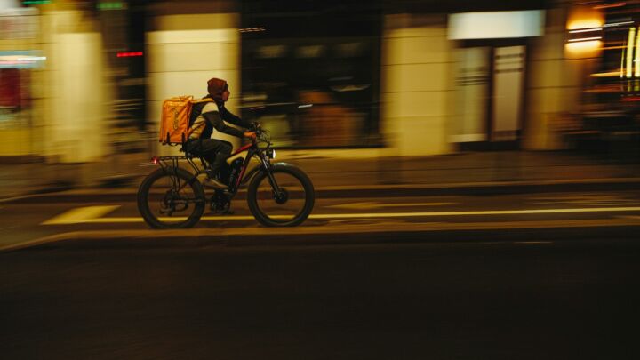 Delivery person rides bicycle through city at night