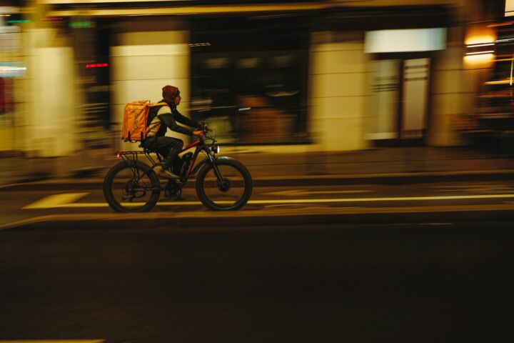 Delivery person rides bicycle through city at night