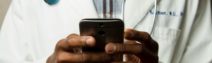 person wearing lavatory gown with green stethoscope on neck using phone while standing