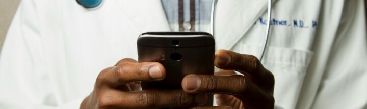 person wearing lavatory gown with green stethoscope on neck using phone while standing
