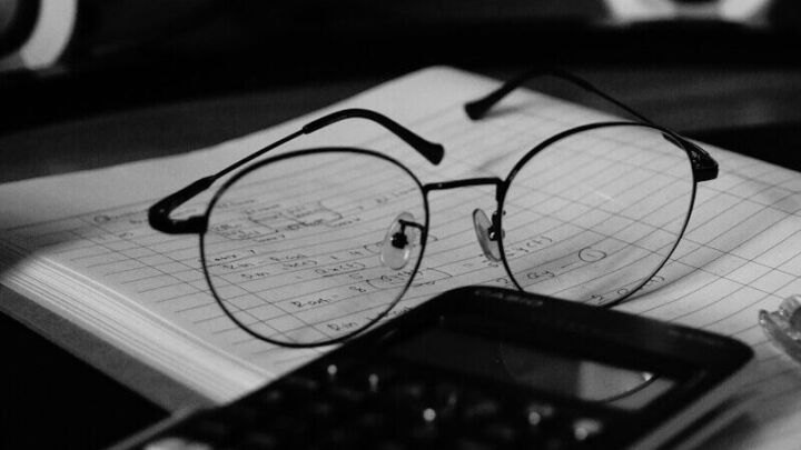 A computer desk with a keyboard, mouse and glasses on it