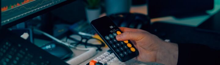 Person using calculator at desk with computer charts.
