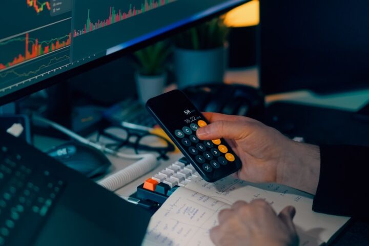 Person using calculator at desk with computer charts.