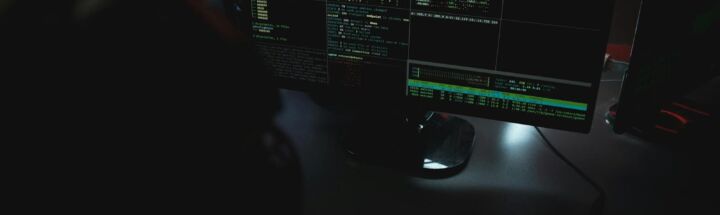 Dark room setup with code displayed on PC monitors highlighting cybersecurity themes.