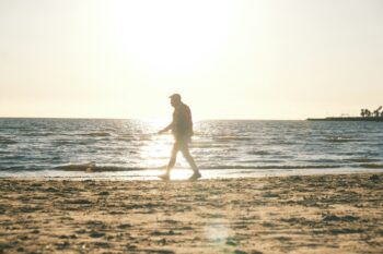 Man walking on a sandy beach at sunset.