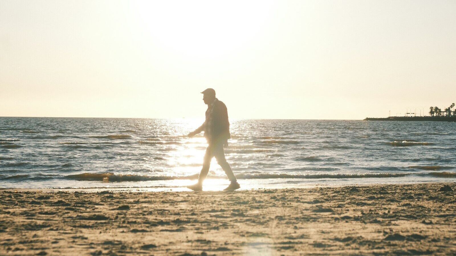 Man walking on a sandy beach at sunset.