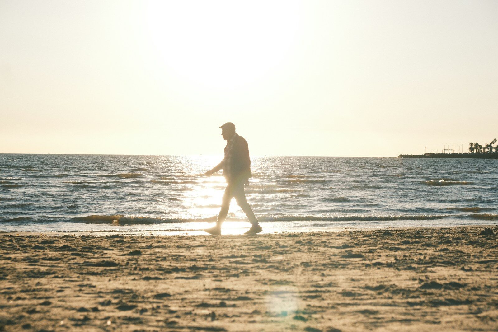 Man walking on a sandy beach at sunset.