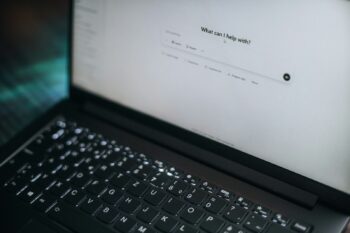 A laptop displays "what can i help with?"