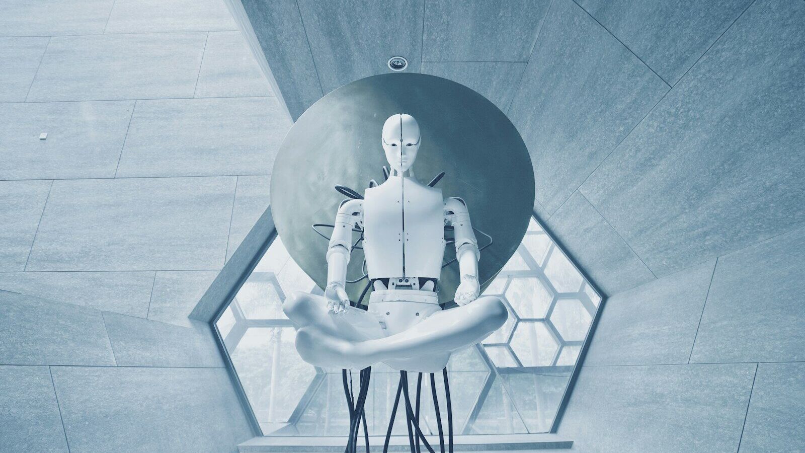 A white humanoid robot in a lotus position against a large circular disc