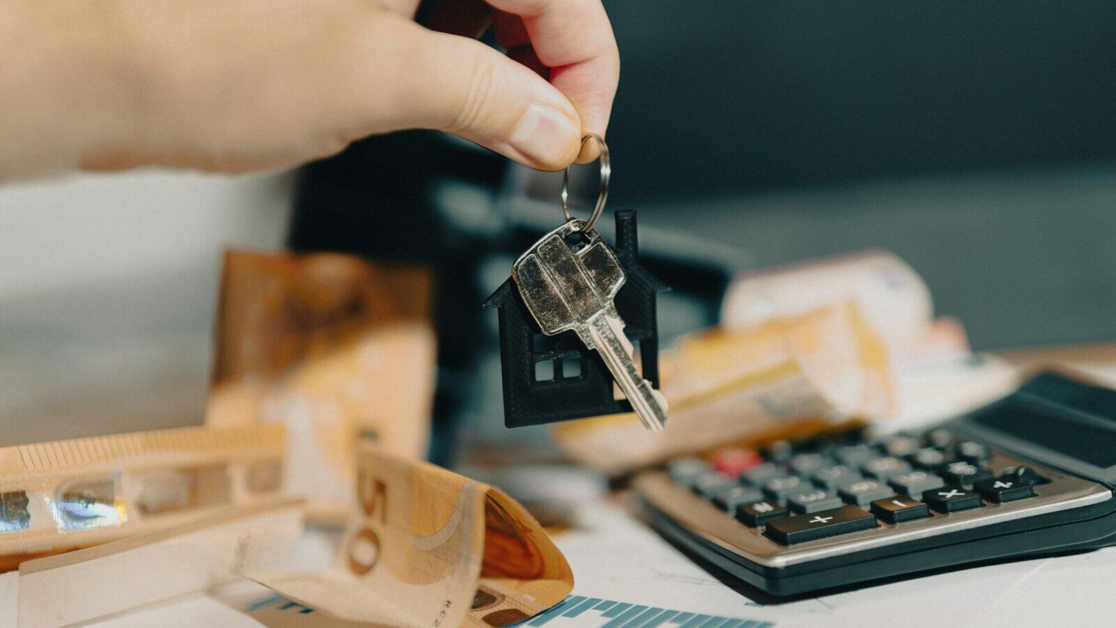 A person holding a house key in front of a calculator